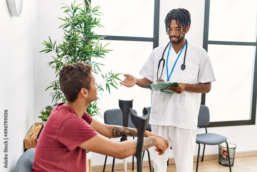 Fototapeta premium Two men physiptherapist and patient having medical consultation using crutches at hospital waiting room