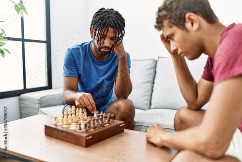 Two men friends playing chess sitting on sofa at home