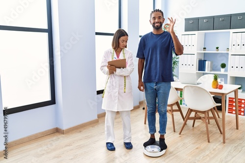 Dietitian at the clinic with client checking weight doing ok sign with fingers, smiling friendly gesturing excellent symbol