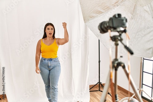 Young beautiful hispanic woman posing as model at photography studio angry and mad raising fist frustrated and furious while shouting with anger. rage and aggressive concept.