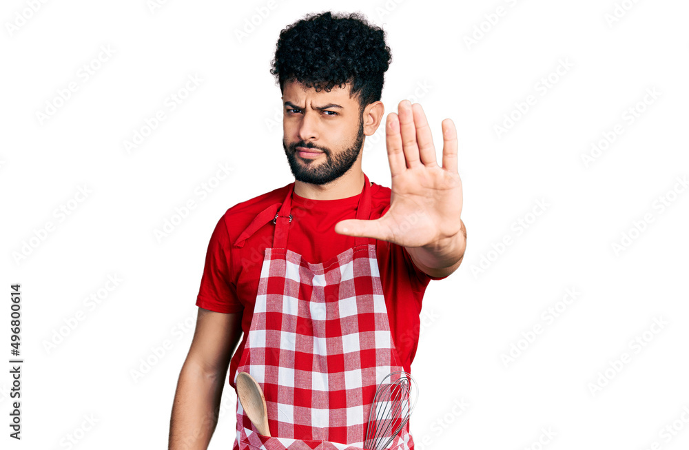 Young arab man with beard wearing cook apron doing stop sing with palm of the hand. warning expression with negative and serious gesture on the face. Young arab man with beard wearing cook apron doing stop sing with palm of the hand. warning expression with negative and serious gesture on the face.