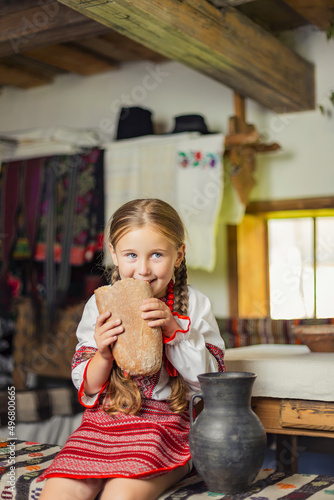 girl in Ukrainian national costume eats bread sitting on a bench in the house