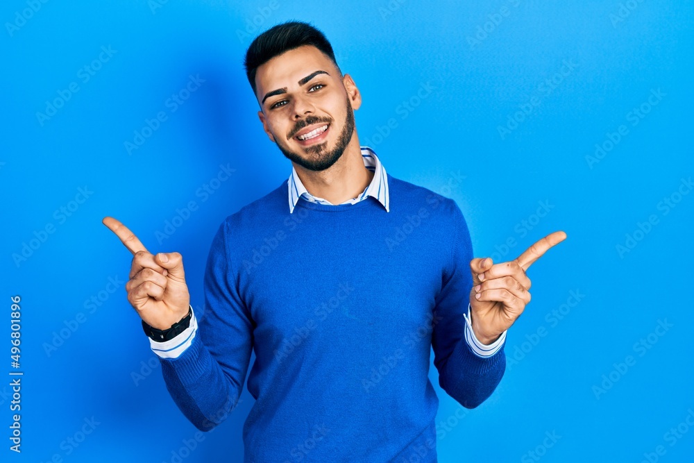 Young hispanic man with beard wearing casual blue sweater smiling confident pointing with fingers to different directions. copy space for advertisement Young hispanic man with beard wearing casual blue sweater smiling confident pointing with fingers to different directions. copy space for advertisement