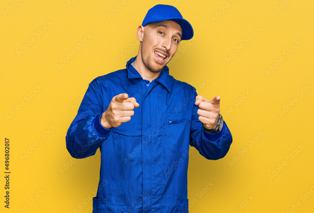 Bald man with beard wearing builder jumpsuit uniform pointing fingers to camera with happy and funny face. good energy and vibes. Bald man with beard wearing builder jumpsuit uniform pointing fingers to camera with happy and funny face. good energy and vibes.