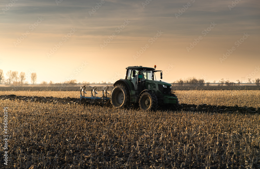 Obraz premium Tractor on the field during sunset.