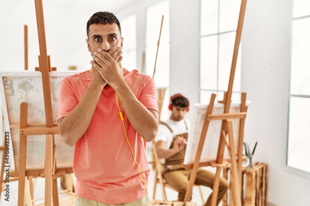Young hispanic man at art studio shocked covering mouth with hands for mistake. secret concept. Young hispanic man at art studio shocked covering mouth with hands for mistake. secret concept.