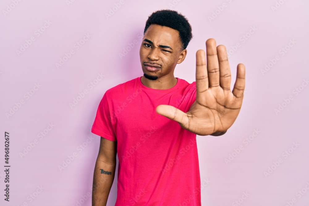 Young african american man wearing casua t shirt doing stop sing with palm of the hand. warning expression with negative and serious gesture on the face. Young african american man wearing casua t shirt doing stop sing with palm of the hand. warning expression with negative and serious gesture on the face.