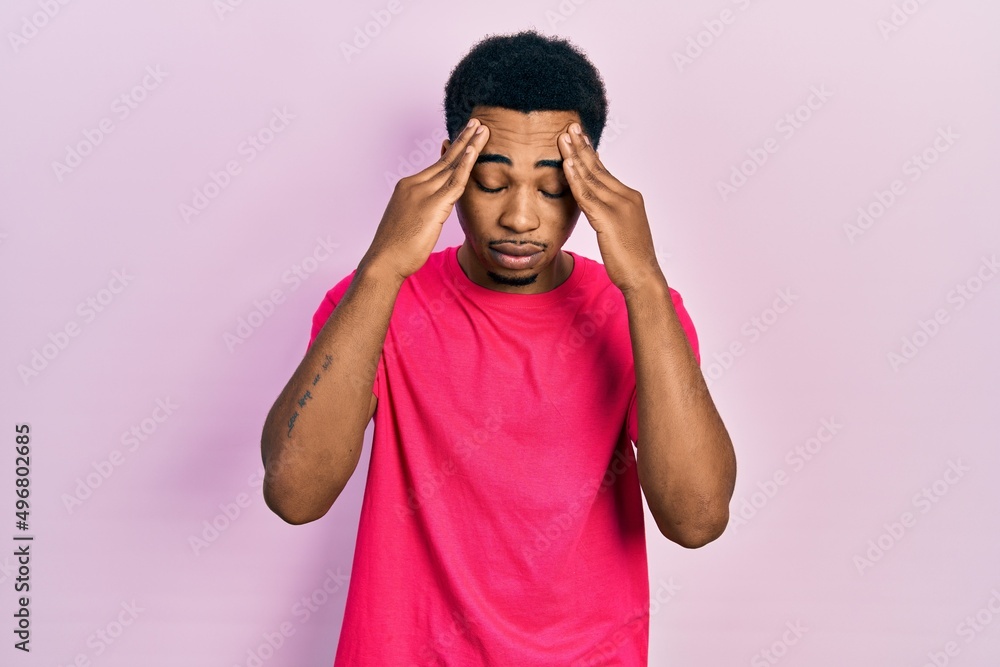 Fototapeta premium Young african american man wearing casua t shirt with hand on head for pain in head because stress. suffering migraine.