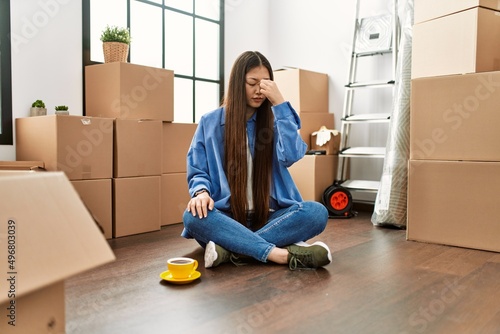 Young chinese girl sitting on the floor at new home tired rubbing nose and eyes feeling fatigue and headache. stress and frustration concept. photo