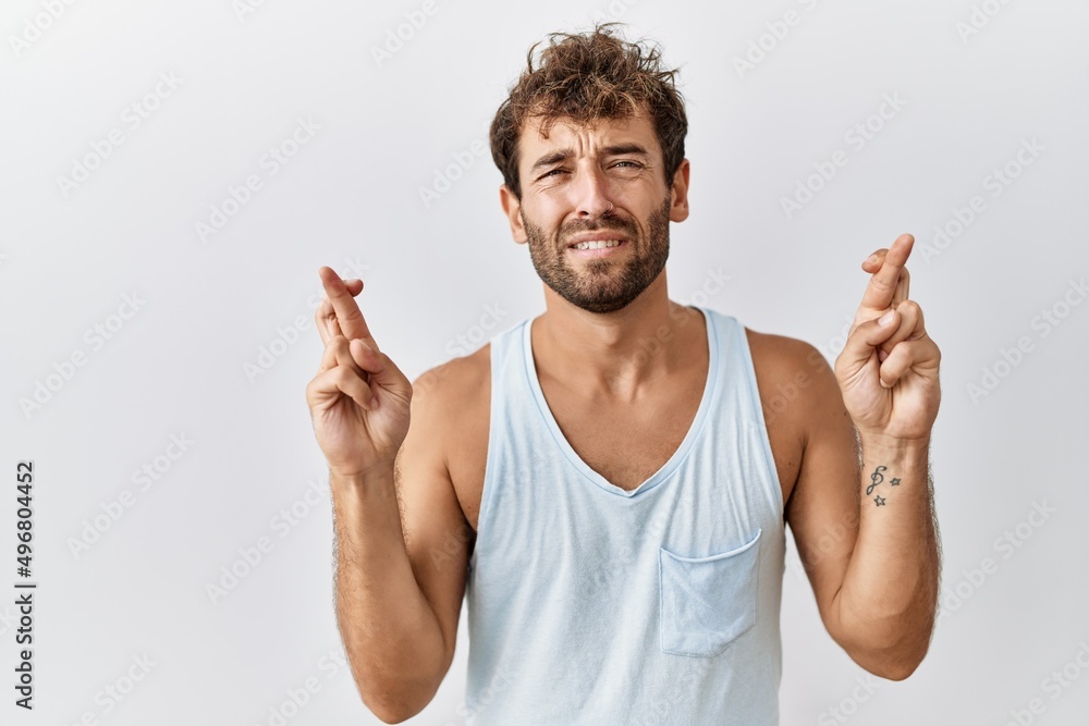 Young handsome man standing over isolated background gesturing finger crossed smiling with hope and eyes closed. luck and superstitious concept. Young handsome man standing over isolated background gesturing finger crossed smiling with hope and eyes closed. luck and superstitious concept.