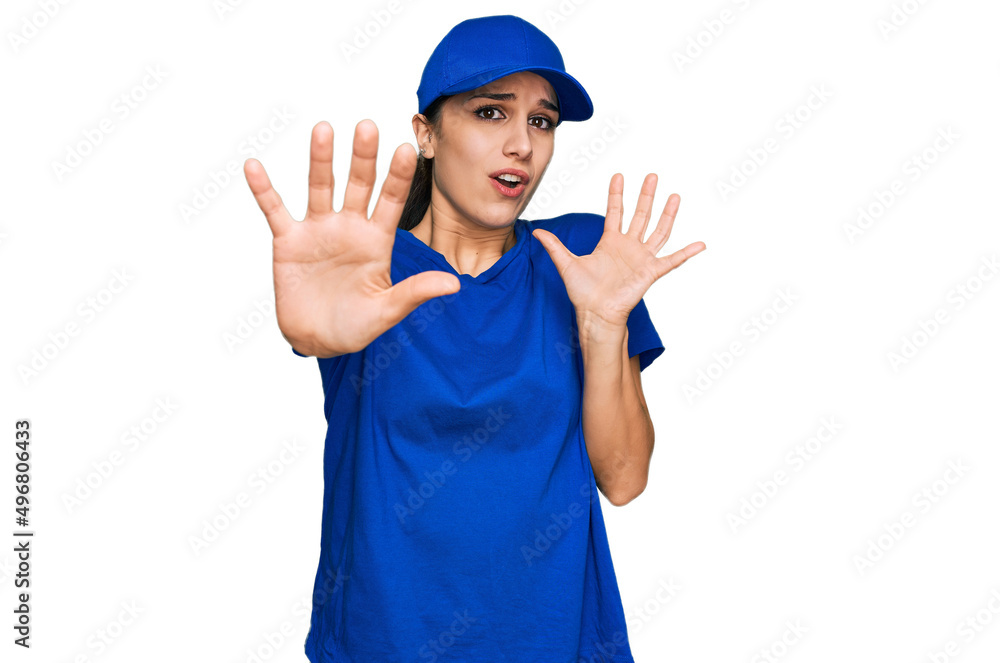 Young hispanic girl wearing delivery courier uniform afraid and terrified with fear expression stop gesture with hands, shouting in shock. panic concept. Young hispanic girl wearing delivery courier uniform afraid and terrified with fear expression stop gesture with hands, shouting in shock. panic concept.