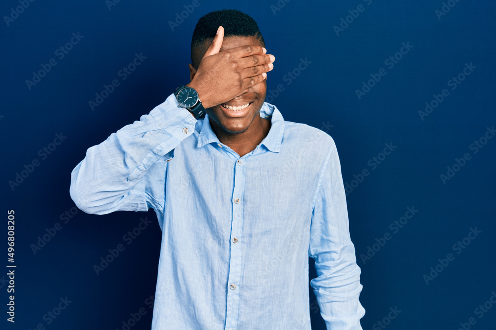 Young african american man wearing casual clothes smiling and laughing with hand on face covering eyes for surprise. blind concept.