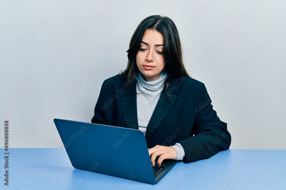 Beautiful hispanic woman working at the office with laptop relaxed with serious expression on face. simple and natural looking at the camera. Beautiful hispanic woman working at the office with laptop relaxed with serious expression on face. simple and natural looking at the camera.