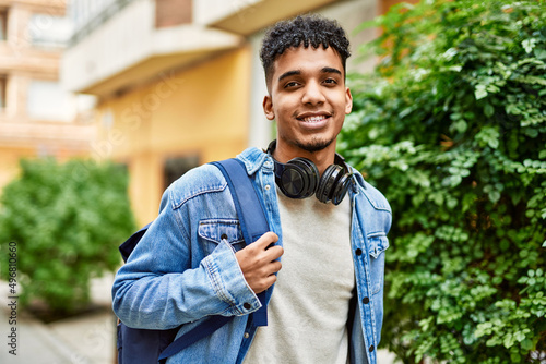 Hispanic young man smiling wearing headphones at the street
