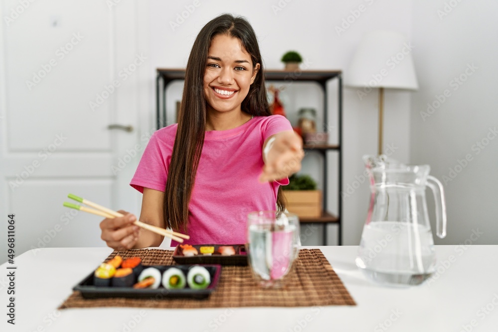 Young brunette woman eating sushi using chopsticks smiling cheerful offering palm hand giving assistance and acceptance. Young brunette woman eating sushi using chopsticks smiling cheerful offering palm hand giving assistance and acceptance.