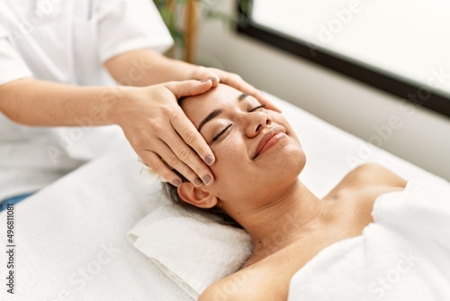 Young latin woman relaxed having face massage at beauty center