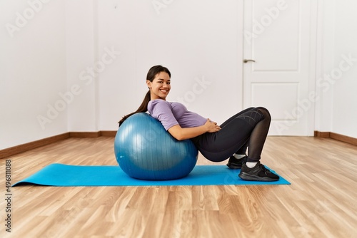 Young latin woman doing abs exercise using fit ball at sport center