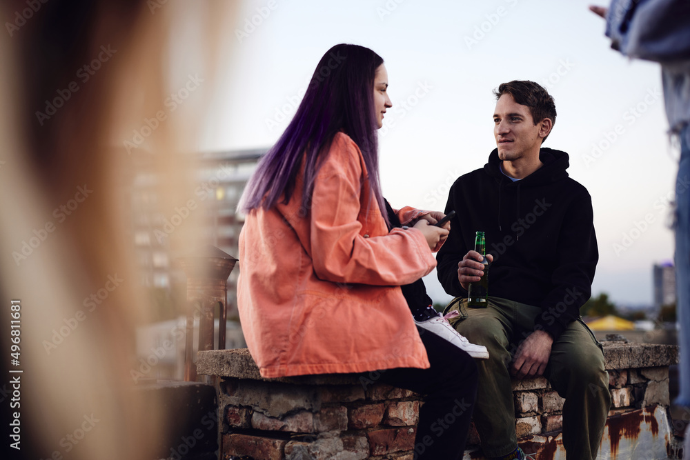 A teenage friends on a rooftop party drinking beer and chatting.