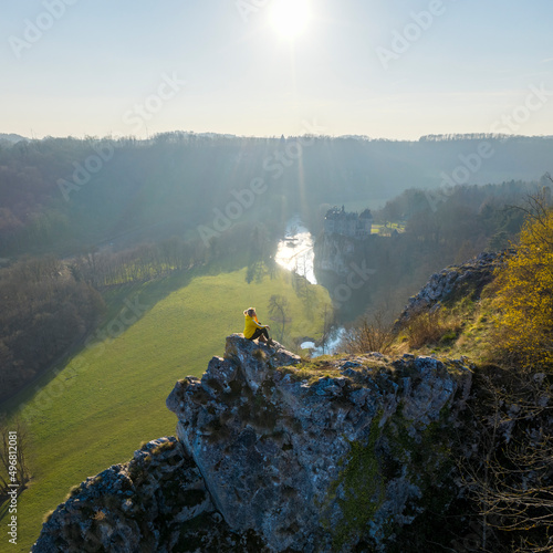 Aerial view of a woman sitting on the rocks with Walzin castle in background at sunset, Dinant, Namur, Belgium. photo