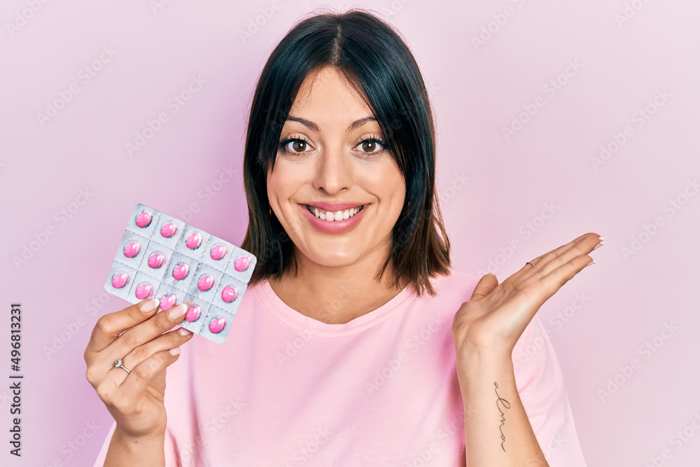 Young hispanic woman holding pills celebrating victory with happy smile and winner expression with raised hands Young hispanic woman holding pills celebrating victory with happy smile and winner expression with raised hands