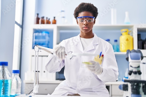Fototapeta Naklejka Na Ścianę i Meble -  African american woman wearing scientist uniform using magnifying glass at laboratory