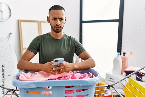 African american man doing laundry using smartphone skeptic and nervous, frowning upset because of problem. negative person.