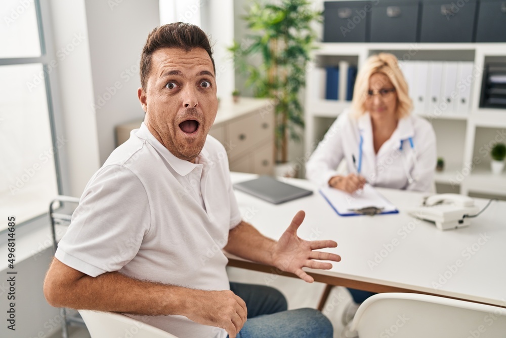 Hispanic man at the doctor scared and amazed with open mouth for surprise, disbelief face