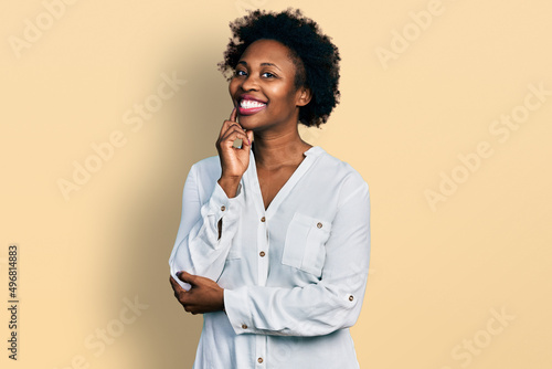 African american woman with afro hair wearing casual white t shirt looking confident at the camera with smile with crossed arms and hand raised on chin. thinking positive.