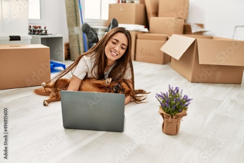 Young hispanic woman using laptop lying on floor hugging dog at new home © Krakenimages.com