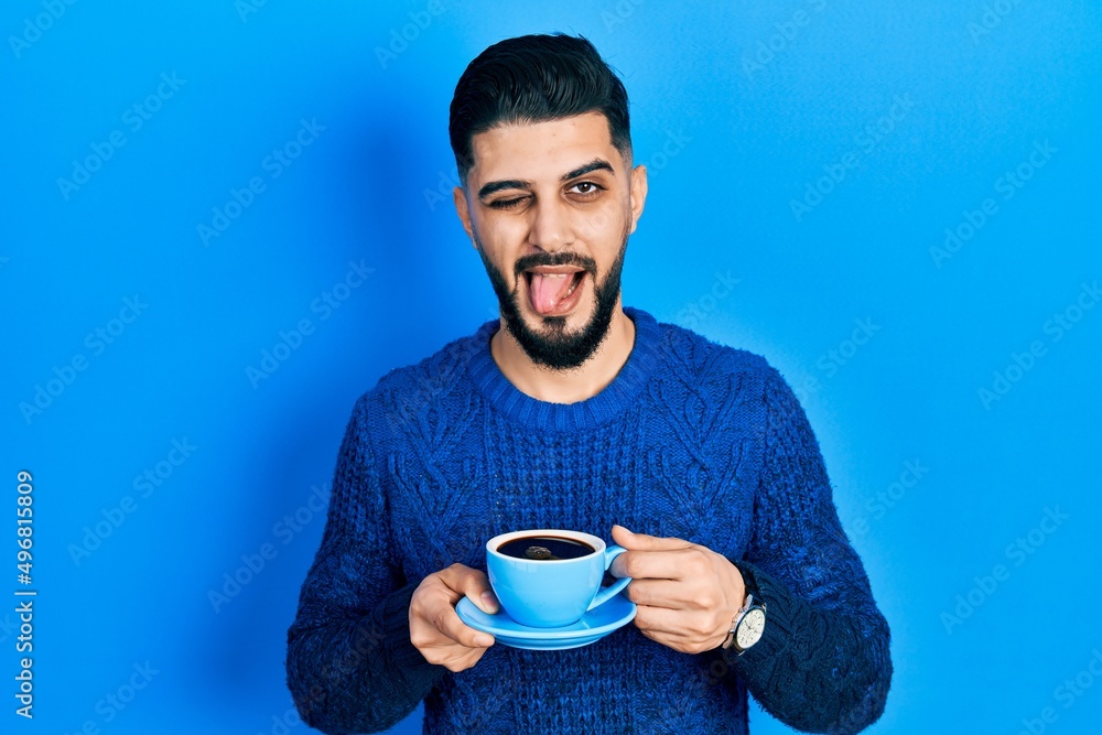 Handsome man with beard drinking a cup of coffee sticking tongue out happy with funny expression. Handsome man with beard drinking a cup of coffee sticking tongue out happy with funny expression.