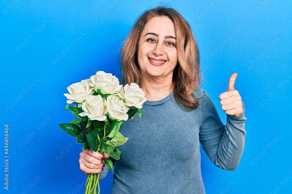 Middle age caucasian woman holding flowers smiling happy and positive, thumb up doing excellent and approval sign Middle age caucasian woman holding flowers smiling happy and positive, thumb up doing excellent and approval sign