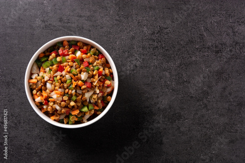 Lentil salad with peppers,onion and carrot in a bowl on black background. Top view. Copy space