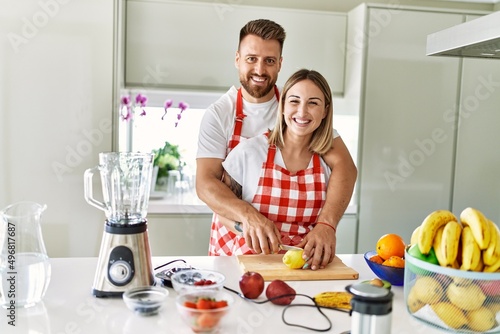 Young couple smiling confident making smoothie hugging each other at kitchen