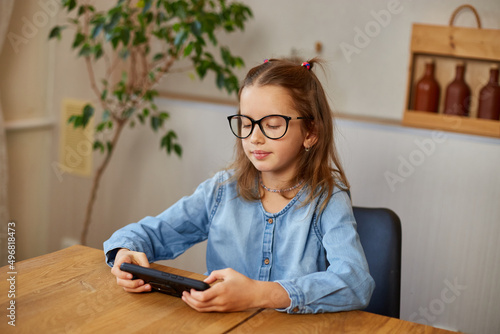 The little girl removes glasses, rubbing eyes tired from play game on smarthon photo