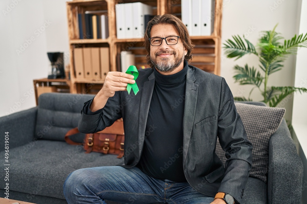 Handsome middle age man holding support green ribbon looking positive and happy standing and smiling with a confident smile showing teeth Handsome middle age man holding support green ribbon looking positive and happy standing and smiling with a confident smile showing teeth