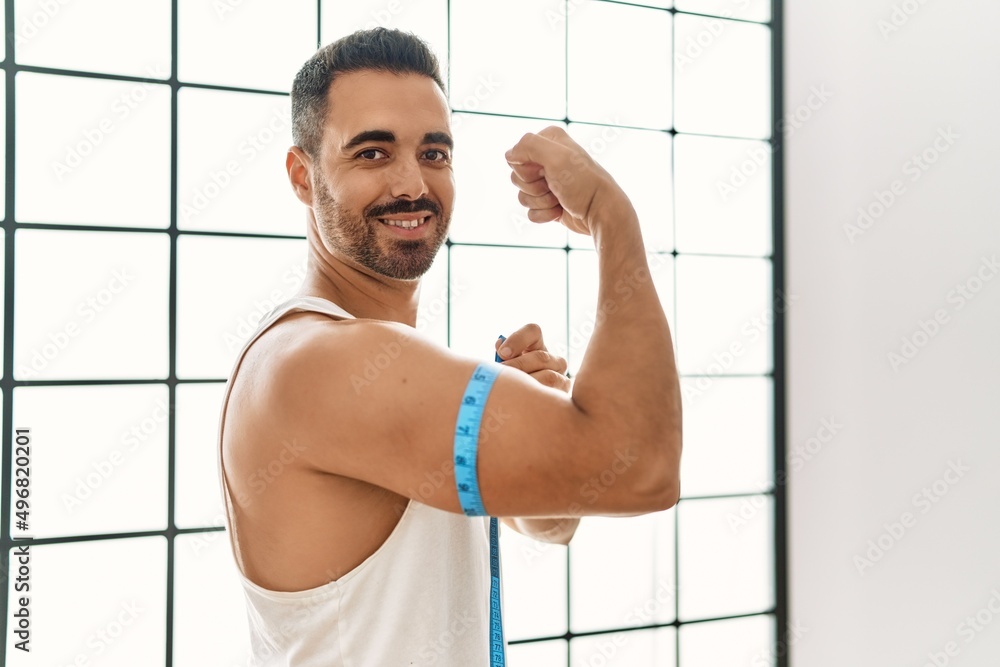 Young hispanic man smiling confident measuring arm muscle with tape measure at sport center Young hispanic man smiling confident measuring arm muscle with tape measure at sport center