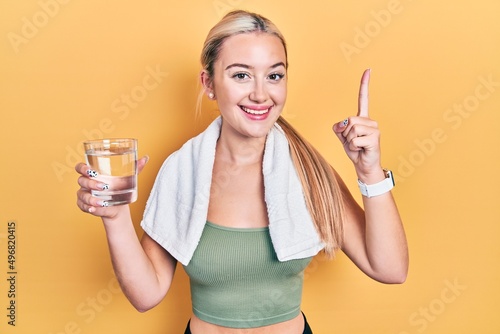 Young blonde girl wearing sportswear drinking glass of water smiling with an idea or question pointing finger with happy face, number one © Krakenimages.com