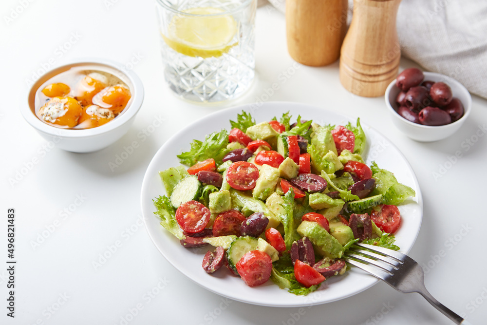 Salad with lettuce, cucumbers, tomatoes, olives and avocados in white plate on the table Salad with lettuce, cucumbers, tomatoes, olives and avocados in white plate on the table