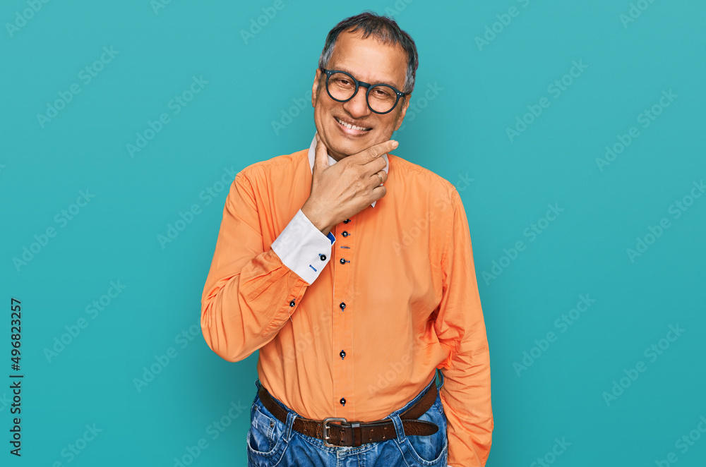 Fototapeta premium Middle age indian man wearing casual clothes and glasses looking confident at the camera smiling with crossed arms and hand raised on chin. thinking positive.