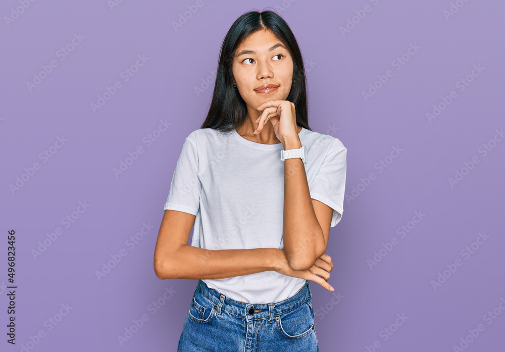 Beautiful young asian woman wearing casual white t shirt with hand on chin thinking about question, pensive expression. smiling and thoughtful face. doubt concept. Beautiful young asian woman wearing casual white t shirt with hand on chin thinking about question, pensive expression. smiling and thoughtful face. doubt concept.
