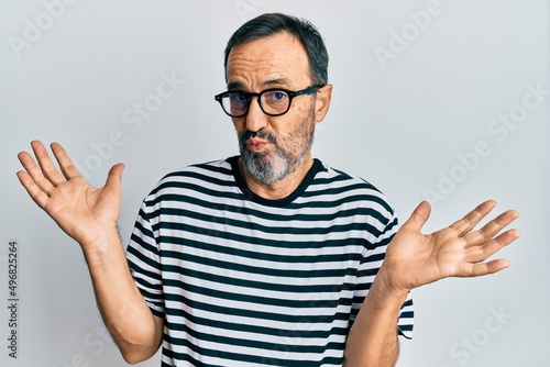 Middle age hispanic man wearing casual clothes and glasses clueless and confused with open arms, no idea and doubtful face.