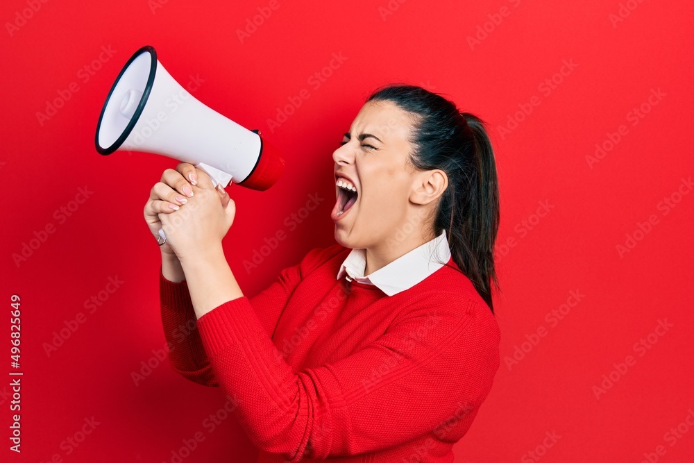 Young brunette woman screaming through megaphone over isolated red background Young brunette woman screaming through megaphone over isolated red background