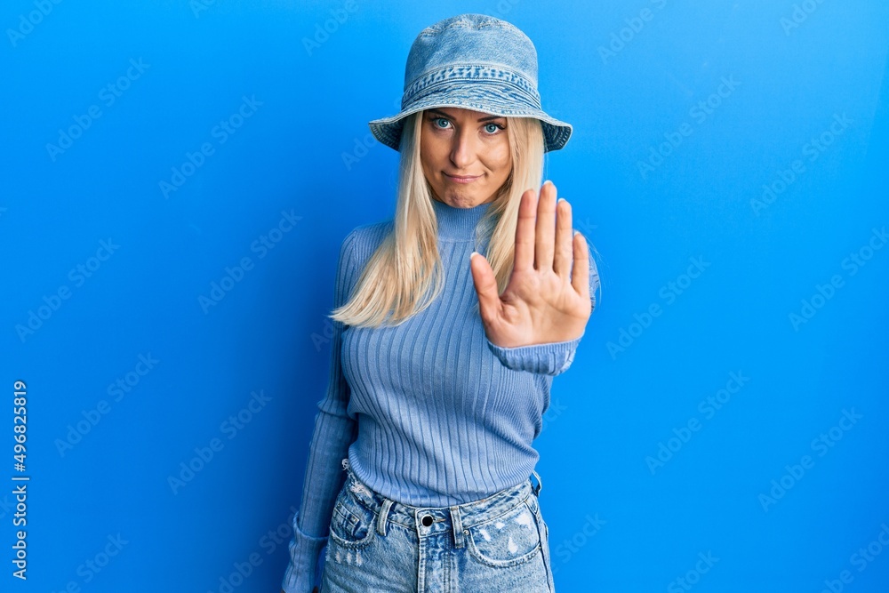 Young blonde woman wearing casual denim hat doing stop sing with palm of the hand. warning expression with negative and serious gesture on the face. Young blonde woman wearing casual denim hat doing stop sing with palm of the hand. warning expression with negative and serious gesture on the face.