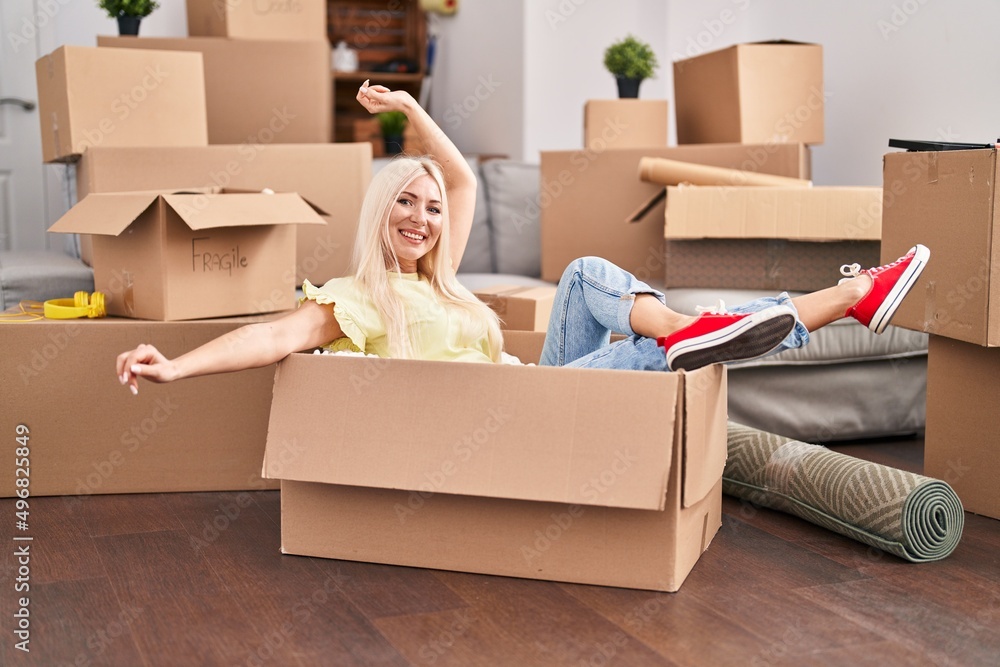 Fototapeta premium Young blonde woman smiling confident sitting in cardboard box at new home