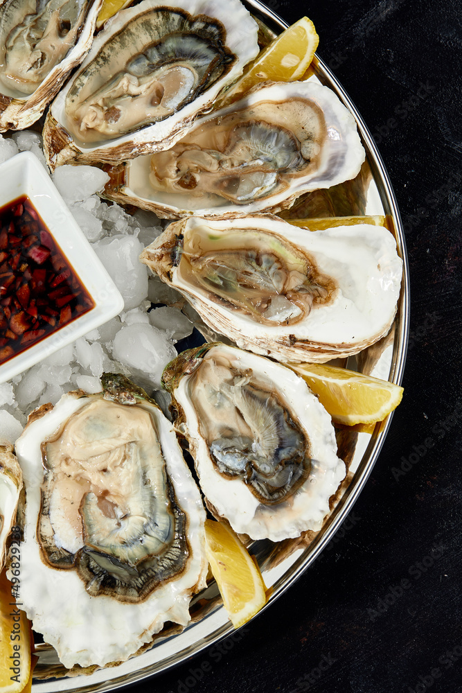 Oysters with lemon served on black round platter. Luxury delicatessen seafood.