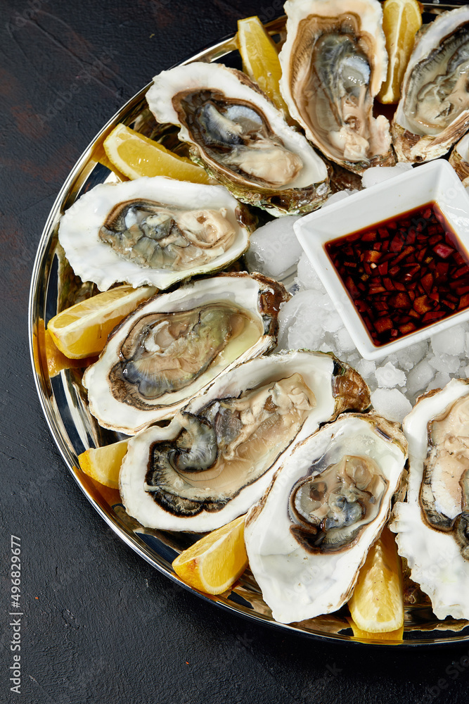 Oysters with lemon served on black round platter. Luxury delicatessen seafood. Oysters with lemon served on black round platter. Luxury delicatessen seafood.