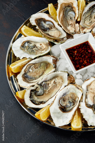 Oysters with lemon served on black round platter. Luxury delicatessen seafood.