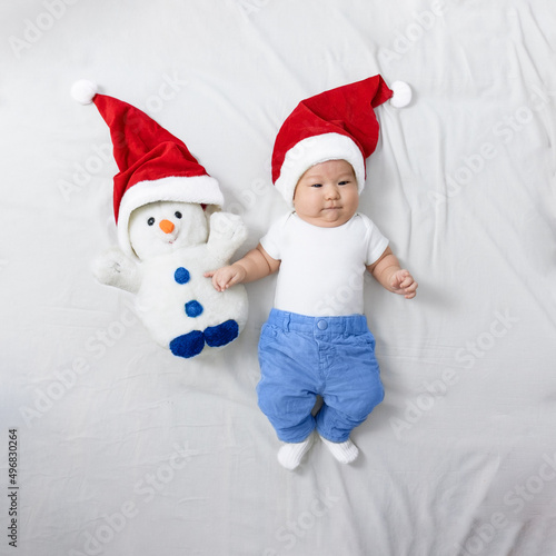 a baby in a santa hat lies on the bed next to a plush toy snowman in a christmas hat. christmas, 