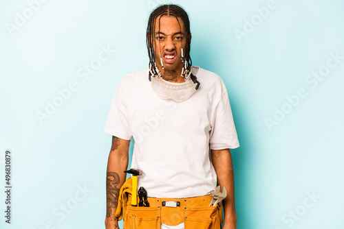 Photos Young mechanic African American man isolated on blue background screaming very angry and aggressive