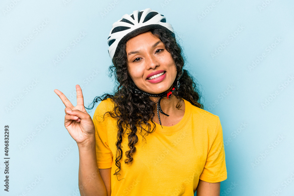 Young hispanic woman wearing a helmet bike isolated on blue background joyful and carefree showing a peace symbol with fingers.